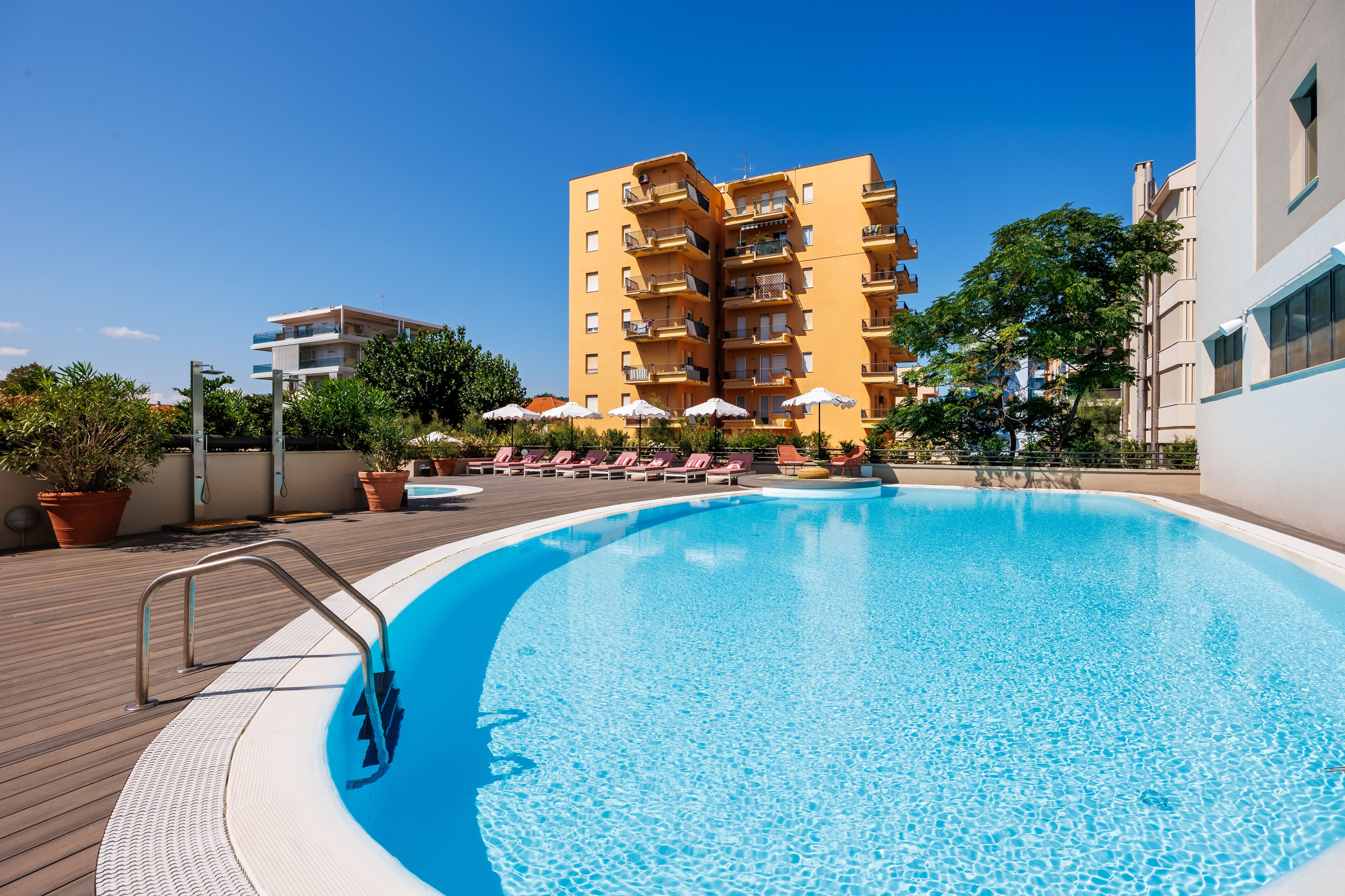 A swimming pool with a wooden deck, lounge chairs, and umbrellas.