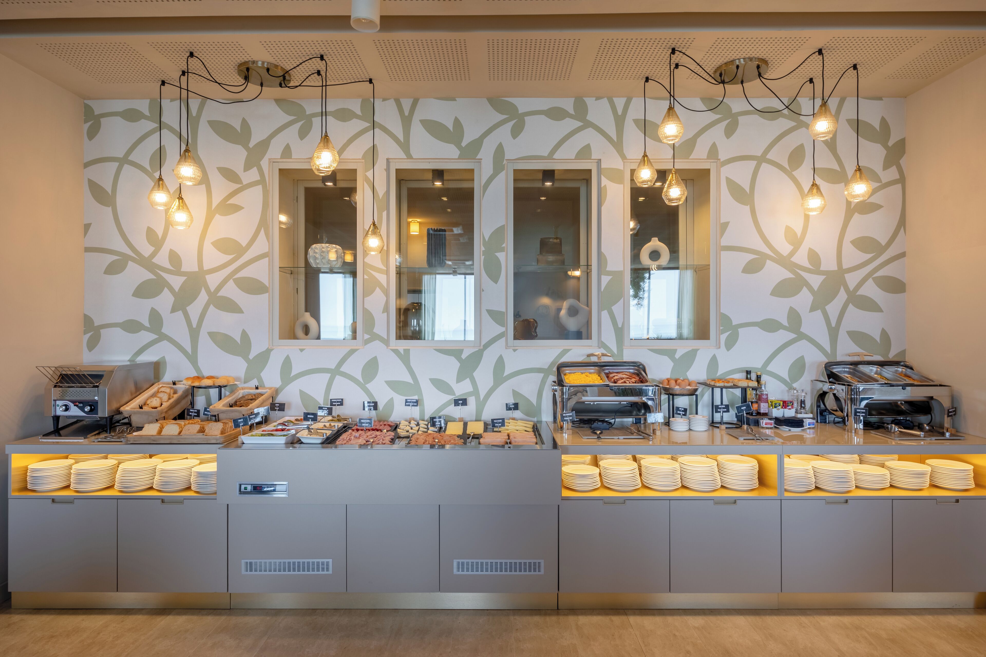 Un comptoir de buffet proposant divers plats et un espace dédié au café, le tout installé devant un mur orné d’un motif de feuilles.