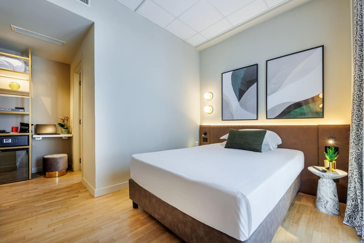 Una habitación de hotel moderna con una cama grande, una mesita de noche con lámpara y un televisor de pared.