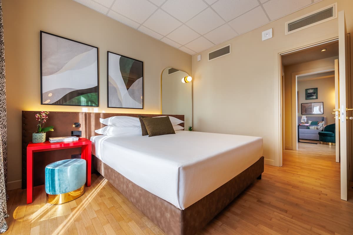 Una habitación de hotel moderna con una cama grande, una mesita de noche roja y un otomán azul.