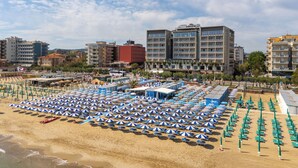 Una playa con hileras de sombrillas azules y blancas, y sillas reclinables verdes.