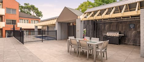 A patio with a table and chairs, a grill, and a gated entrance.