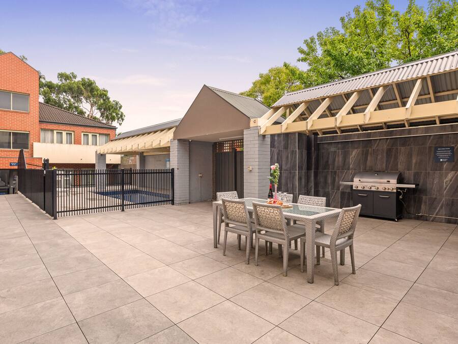 A patio with a table and chairs, a grill, and a gated entrance.