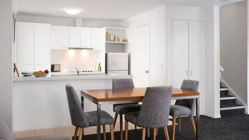 A compact kitchen with white cabinets, a wooden dining table, and four grey chairs.