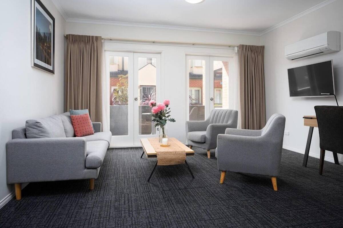 Una sala de estar moderna con un sofá gris, sillones, una mesa de centro y un televisor.