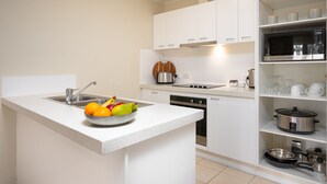 Uma cozinha moderna com armários brancos, forno embutido e uma pequena ilha com uma fruteira.