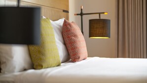 Cama bem arrumada com almofadas estampadas e uma luminária moderna fixada na parede.