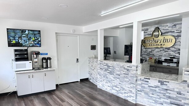 A hotel lobby with a kitchen area, a security camera system, and a sign for 'Masters Inn Economy'. - Masters Inn Atlanta - Doraville at I-85 & 285 (Doraville)