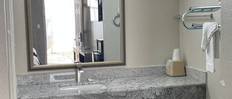 A bathroom with a marble sink, a mirror with a gold frame, a towel rack, and a soap dispenser.