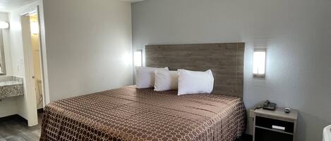 A hotel room with a large bed, a nightstand, a mirror, and a bathroom visible through an open door.