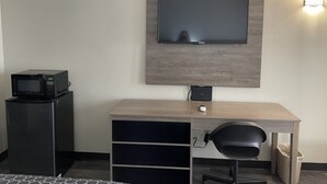 A compact room with a flat-screen TV mounted on the wall, a small black microwave on a stand, a desk with a chair, and a trash bin. - Masters Inn Atlanta - Doraville at I-85 & 285 (Doraville)