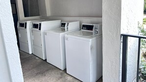 A laundry room with four white washing machines and a dryer, arranged in a row. - Masters Inn Atlanta - Doraville at I-85 & 285 (Doraville)