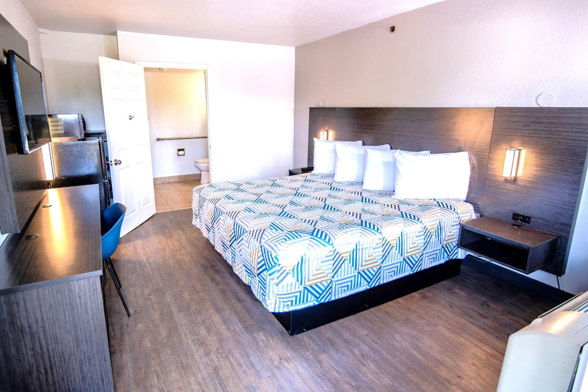 Habitación de hotel con cama, mesita de noche, lámpara y vistas al baño.