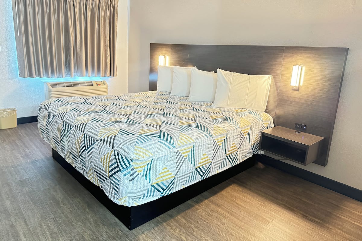 Habitación de hotel moderna con una cama grande, dos mesitas de noche, cabecero con luces empotradas y una ventana con cortinas.