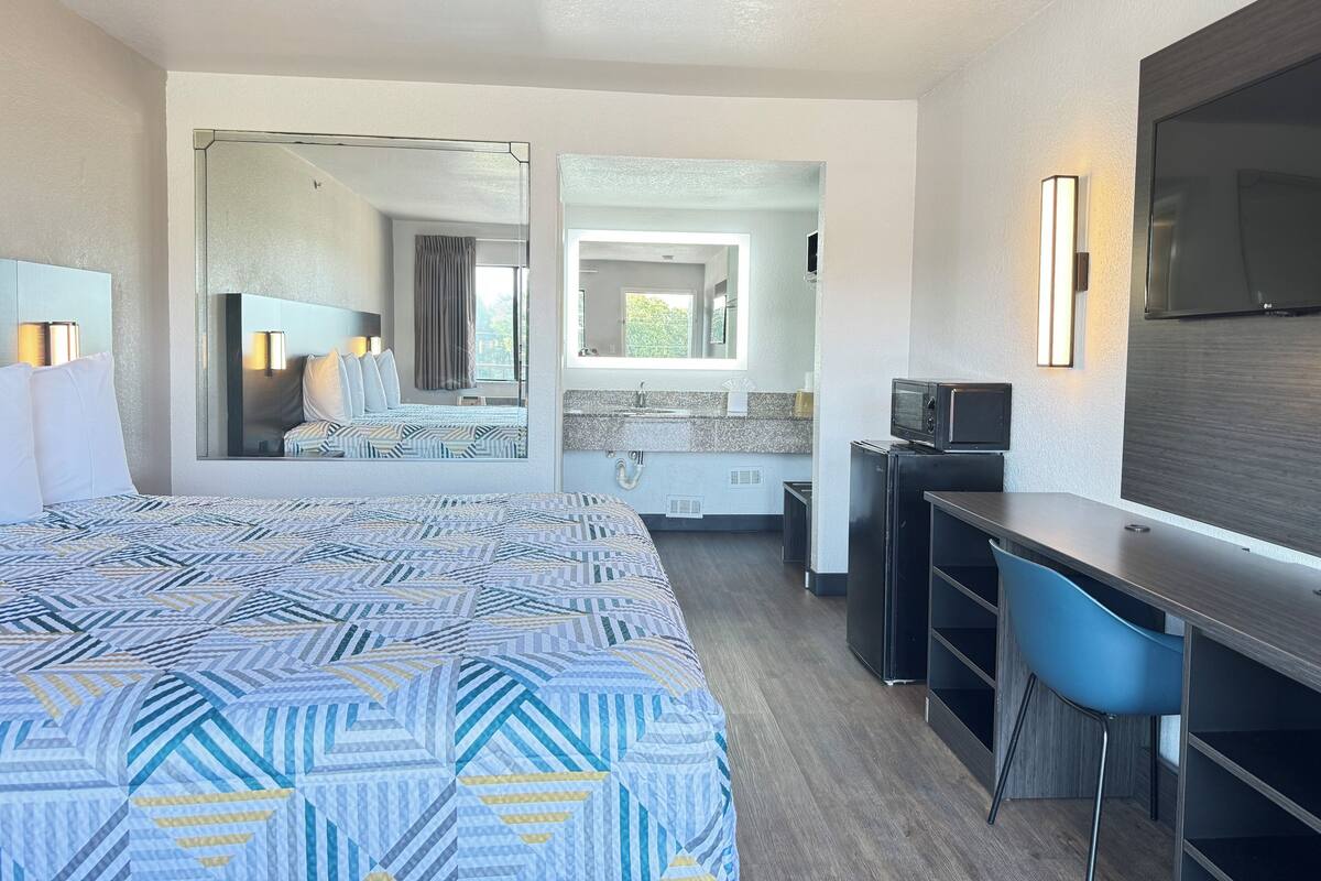 Una habitación de hotel con una cama grande, un escritorio, un televisor y un espejo.