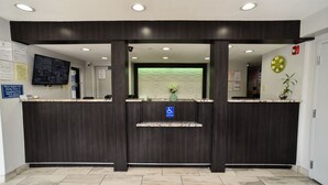 A reception desk with a digital screen, a clock, and a plant. - Masters Inn Tucker (Decatur)