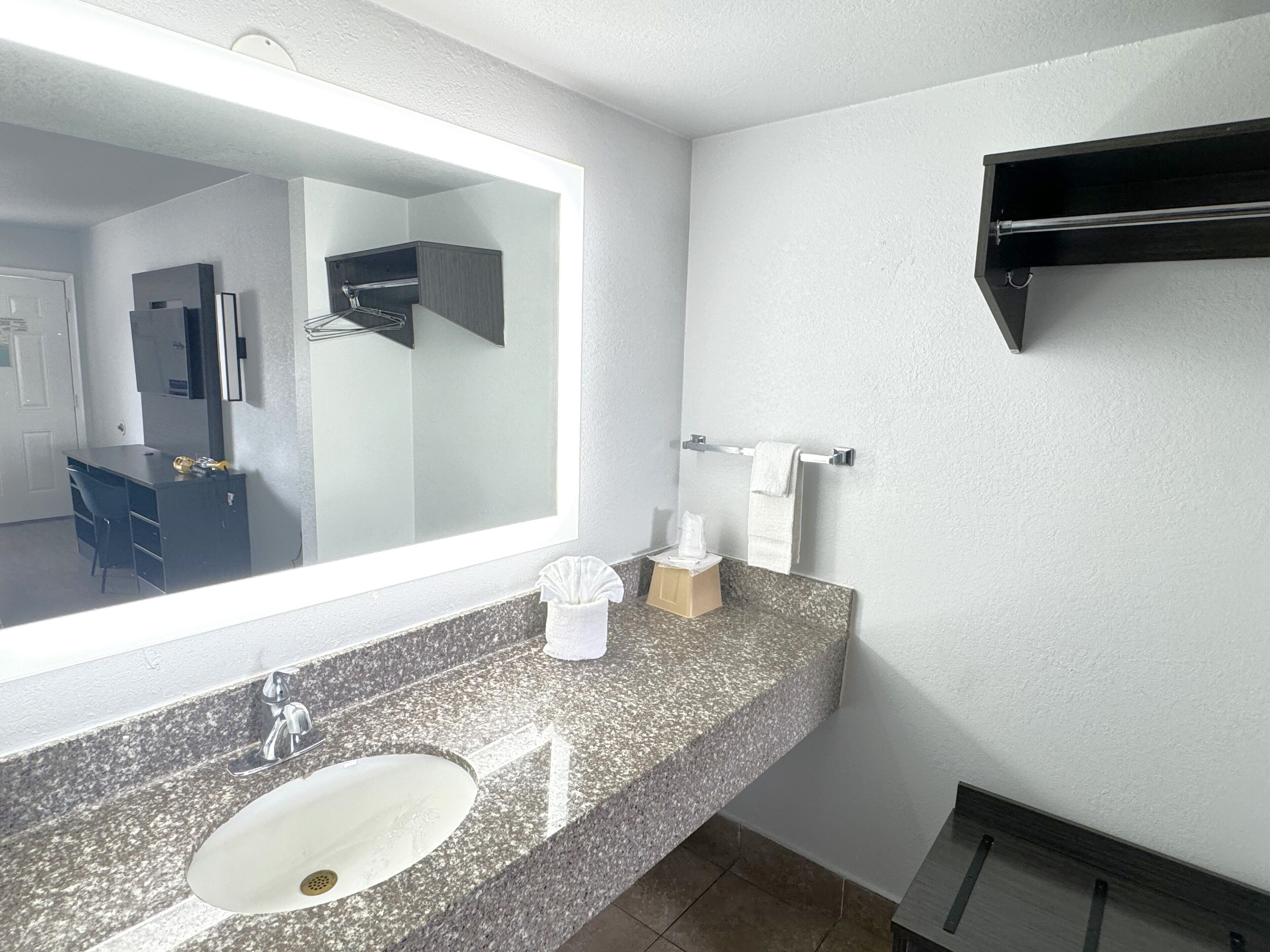 A bathroom with a granite countertop, a sink, a mirror, a towel rack, and a towel dispenser.