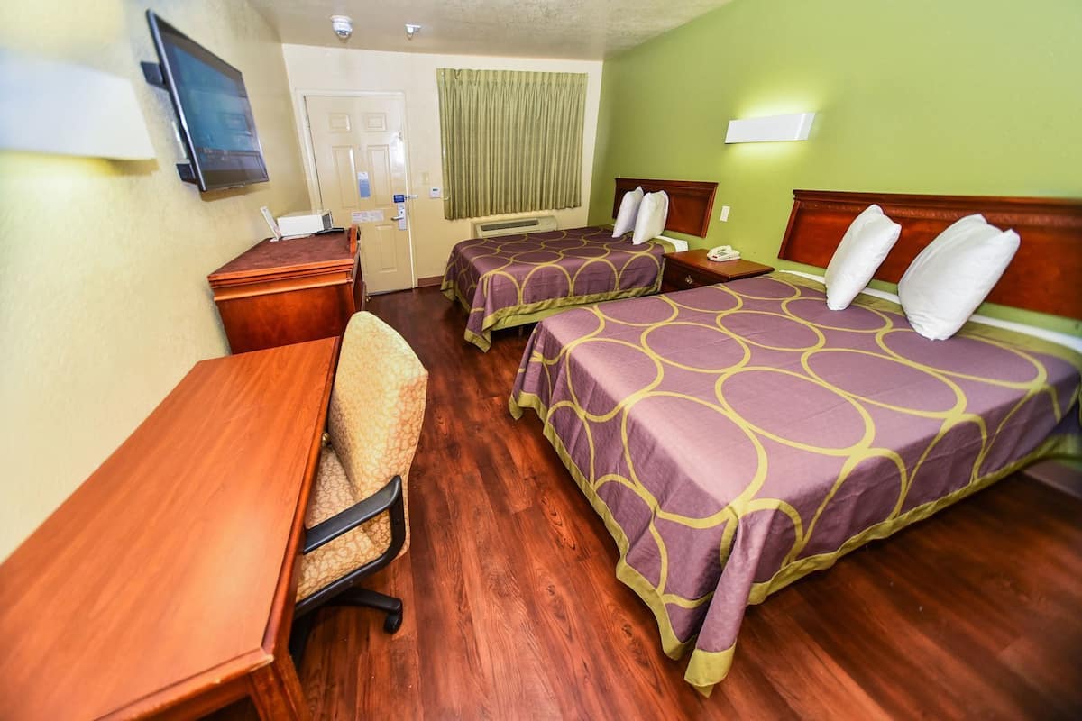 Habitación de hotel con dos camas, un escritorio, una silla, un televisor y una ventana con cortinas.