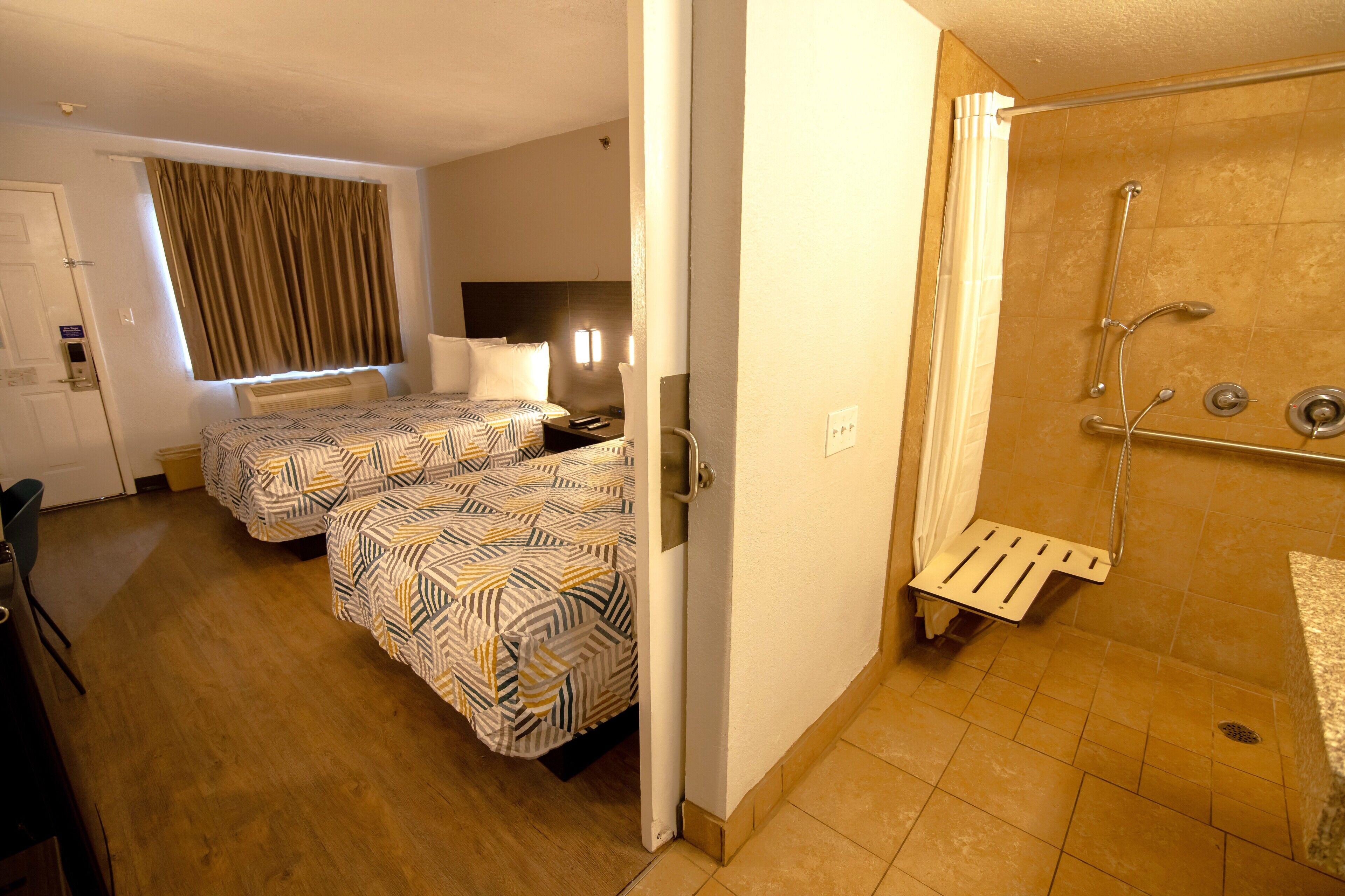 A hotel room with two beds, a shower, and a small desk.
