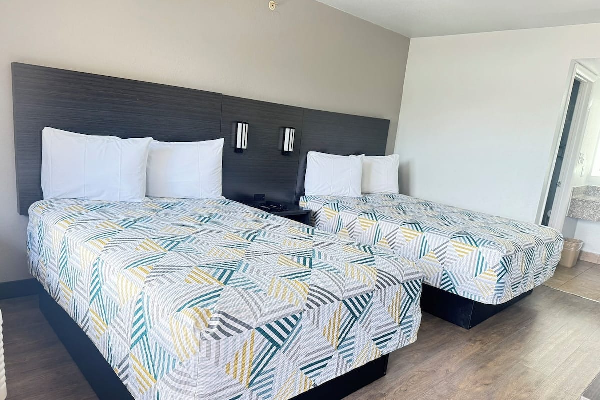 Una cama doble con una colcha de estampado geométrico y dos almohadas blancas.