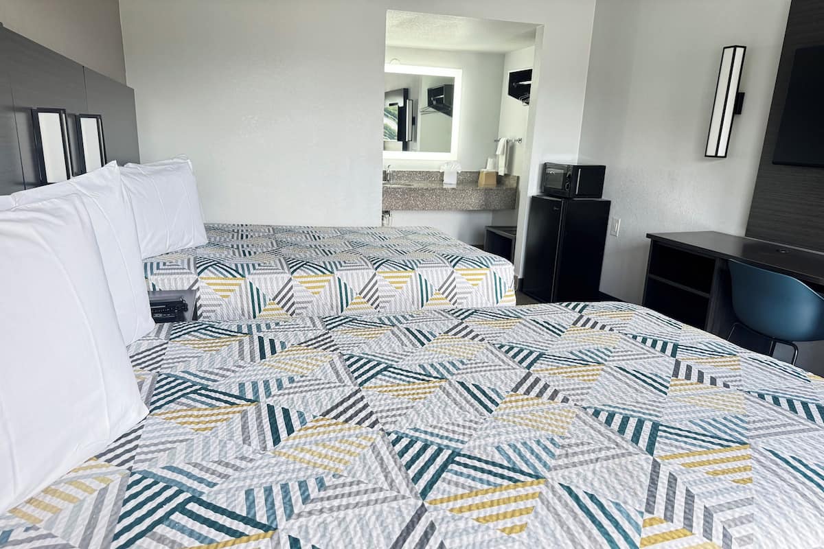 Una habitación de hotel con dos camas, un escritorio, una silla, microondas y una pequeña kitchenette.