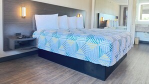 A modern hotel room with a large bed, a nightstand with a lamp, and a mirror above the bed. - Masters Inn Tucker (Decatur)