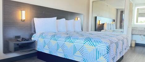 A modern hotel room with a large bed, a nightstand with a lamp, and a mirror above the bed.