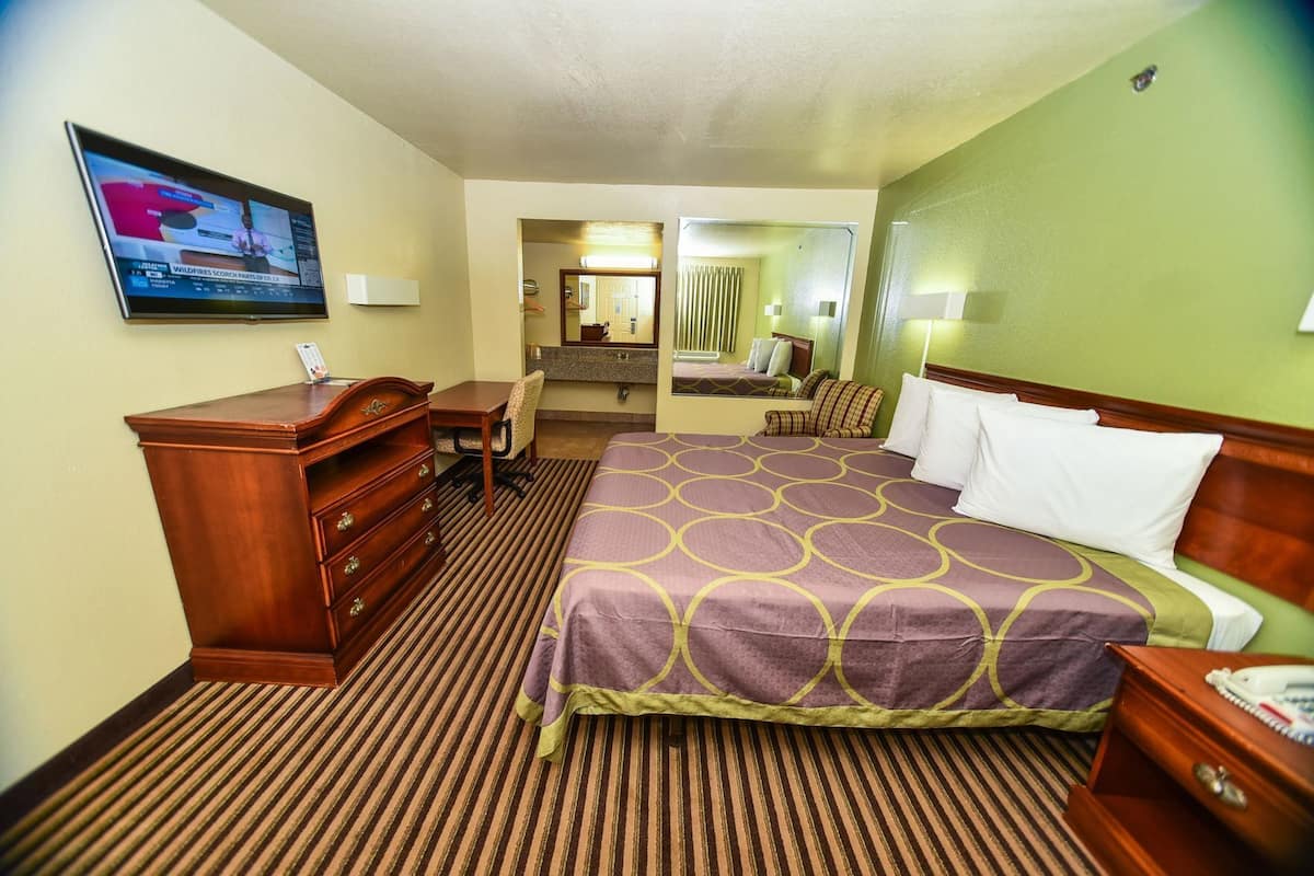 Una habitación de hotel con cama, escritorio, cómoda, espejo y televisor.