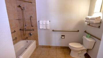 A bathroom with a bathtub, toilet, and shower with grab bars.