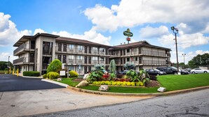 A multi-story motel with a landscaped front yard, a sign indicating it is a Masters Inn, and a parking area with several cars. - Masters Inn Tucker (Decatur)
