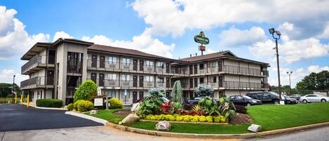 Un motel de varios pisos con un jardín delantero ajardinado, un letrero que indica que es un Masters Inn y un área de estacionamiento con varios autos.