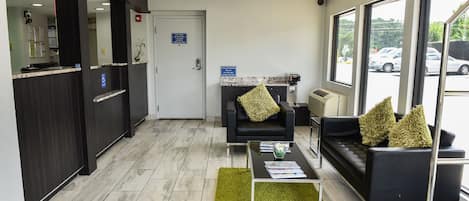 A reception area with a reception desk, black sofas, a coffee table, and a large window offering a view of parked cars outside.