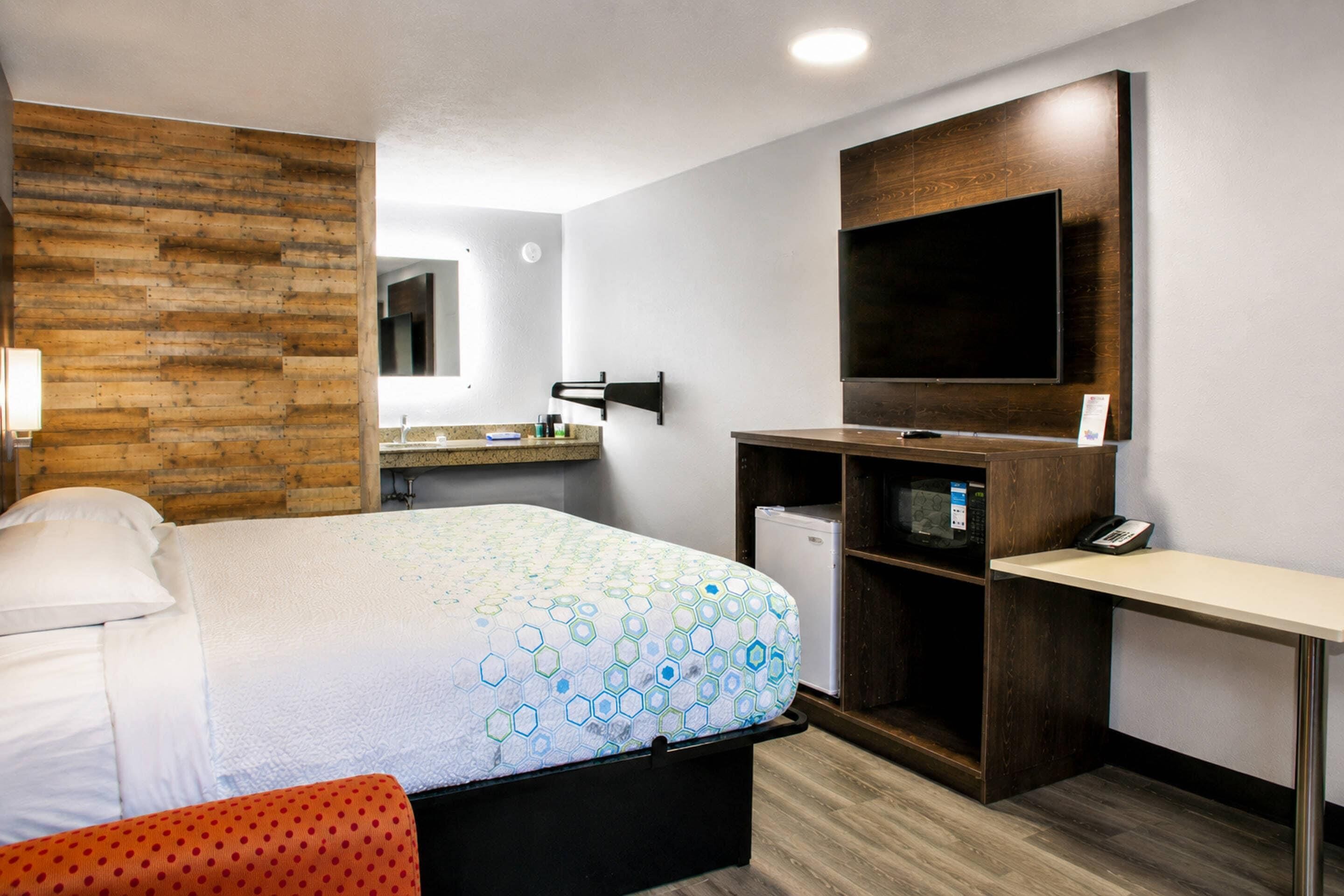 A hotel room with a bed, a desk, a television, and a small refrigerator.