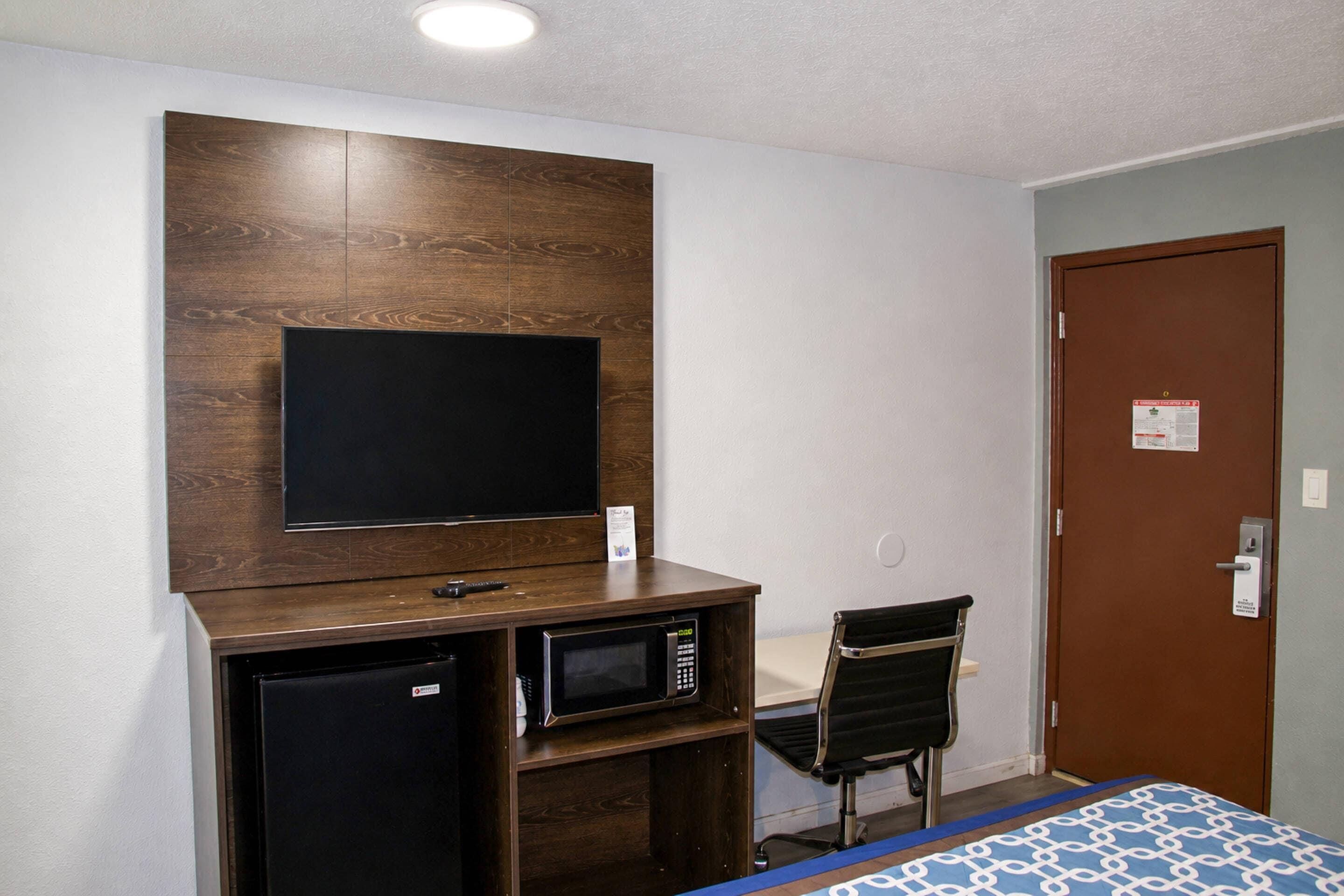 Une chambre comprenant un lit, un bureau avec un ordinateur et un écran, un four à micro-ondes et une chaise.