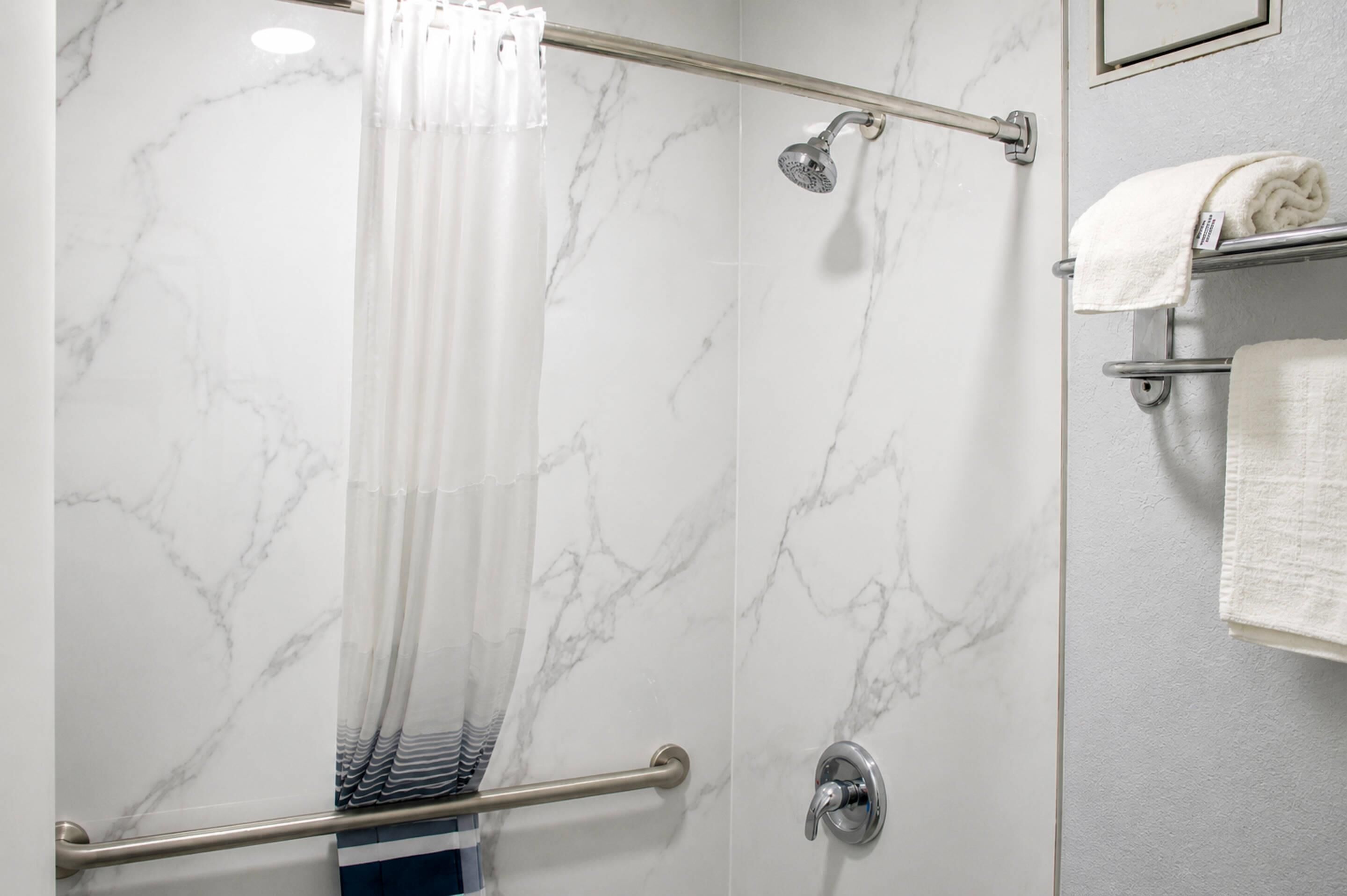 A shower with a marble wall, a glass door, and a towel rack with towels.