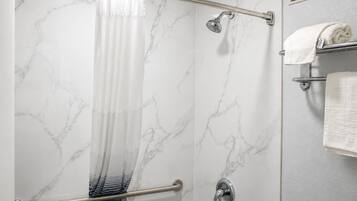 A shower with a marble wall, a glass door, and a towel rack with towels.