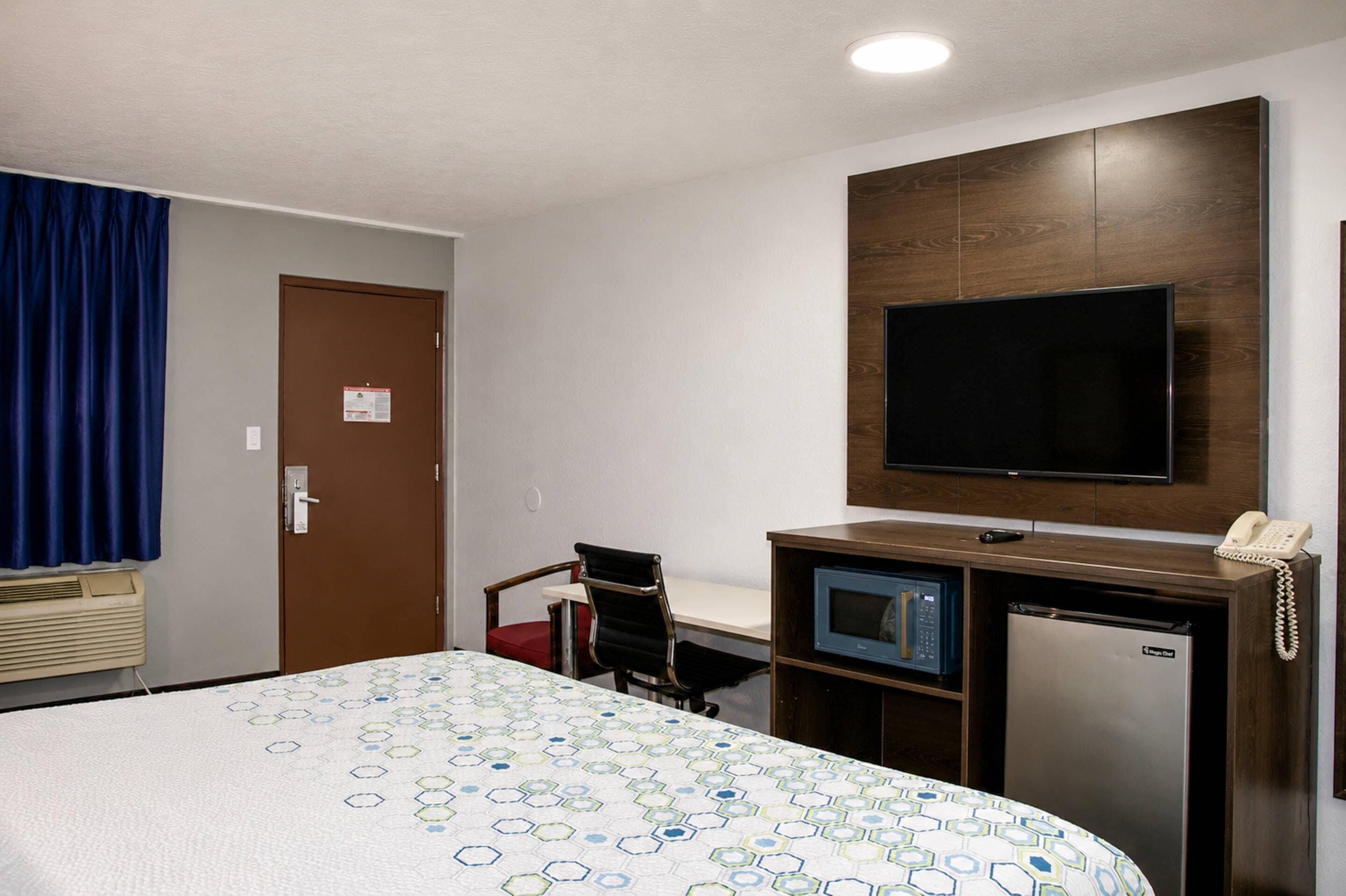 A hotel room with a bed, a desk with a computer, a television, a microwave, and a telephone.