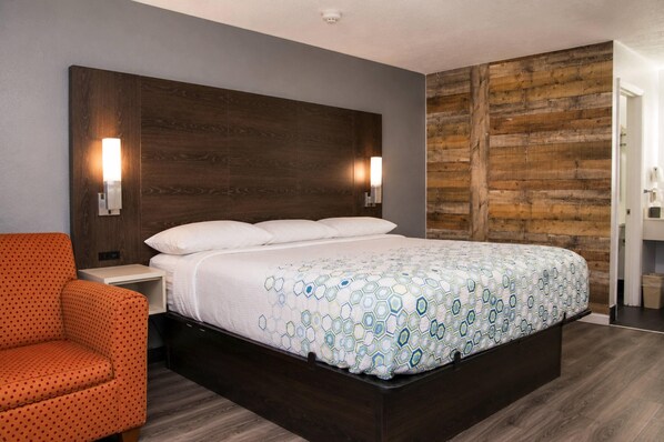 A hotel room with a large bed, two bedside lamps, a wooden headboard, and a polka-dotted armchair.
