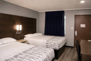 A hotel room with two beds, a desk, a chair, a window with curtains, and a door with a sign. - Masters Inn Augusta at Washington Road (Augusta)