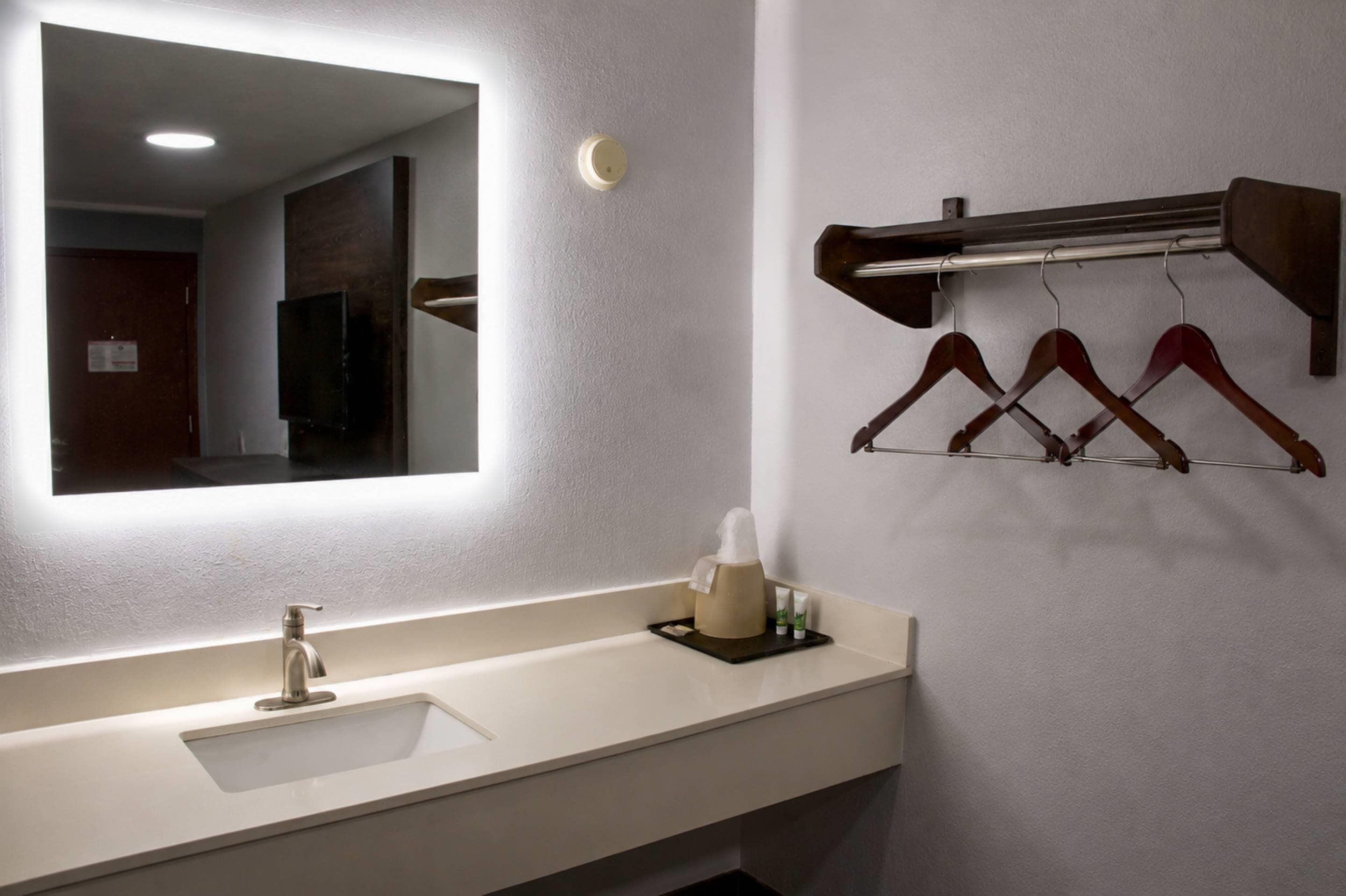 Uma casa de banho de hotel com um espelho grande, uma pia e um porta-toalhas com ganchos.