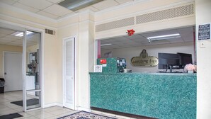Un'area reception con un bancone in marmo verde, un cartello con scritto 'Non ammessi animali' e un cartello con il nome 'Masters Inn', oltre a un televisore.