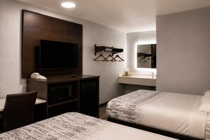 Ein Hotelzimmer mit zwei Betten, einem Schreibtisch mit Fernseher, einem Spiegel und einem kleinen Badezimmer.