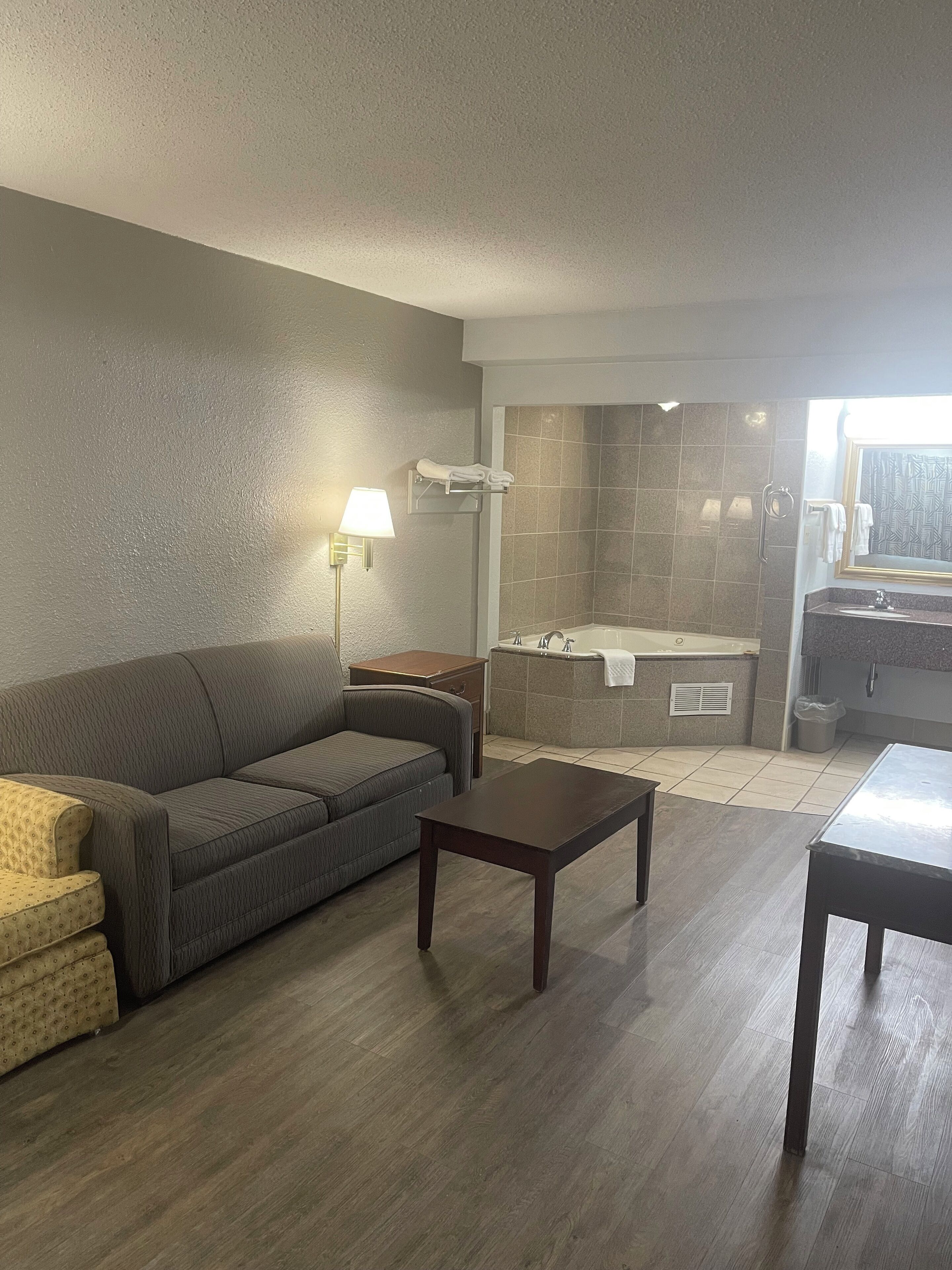 A living room with a sofa, a coffee table, a lamp, and a view of a bathroom with a bathtub and a shower.