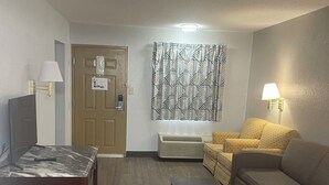 Un soggiorno arredato con un divano, due tavolini, un pannello decorativo a parete e una porta con un cartello.