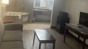 Un ambiente compatto con divano, un piccolo tavolo, televisione e angolo cottura con lavandino e specchio.