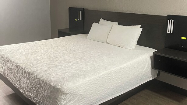 Una camera d'albergo moderna con un letto grande, una testiera scura e due comodini con lampade.