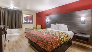 Quarto de hotel com uma cama grande, uma escrivaninha com cadeira, televisão e uma parede com detalhe em vermelho.