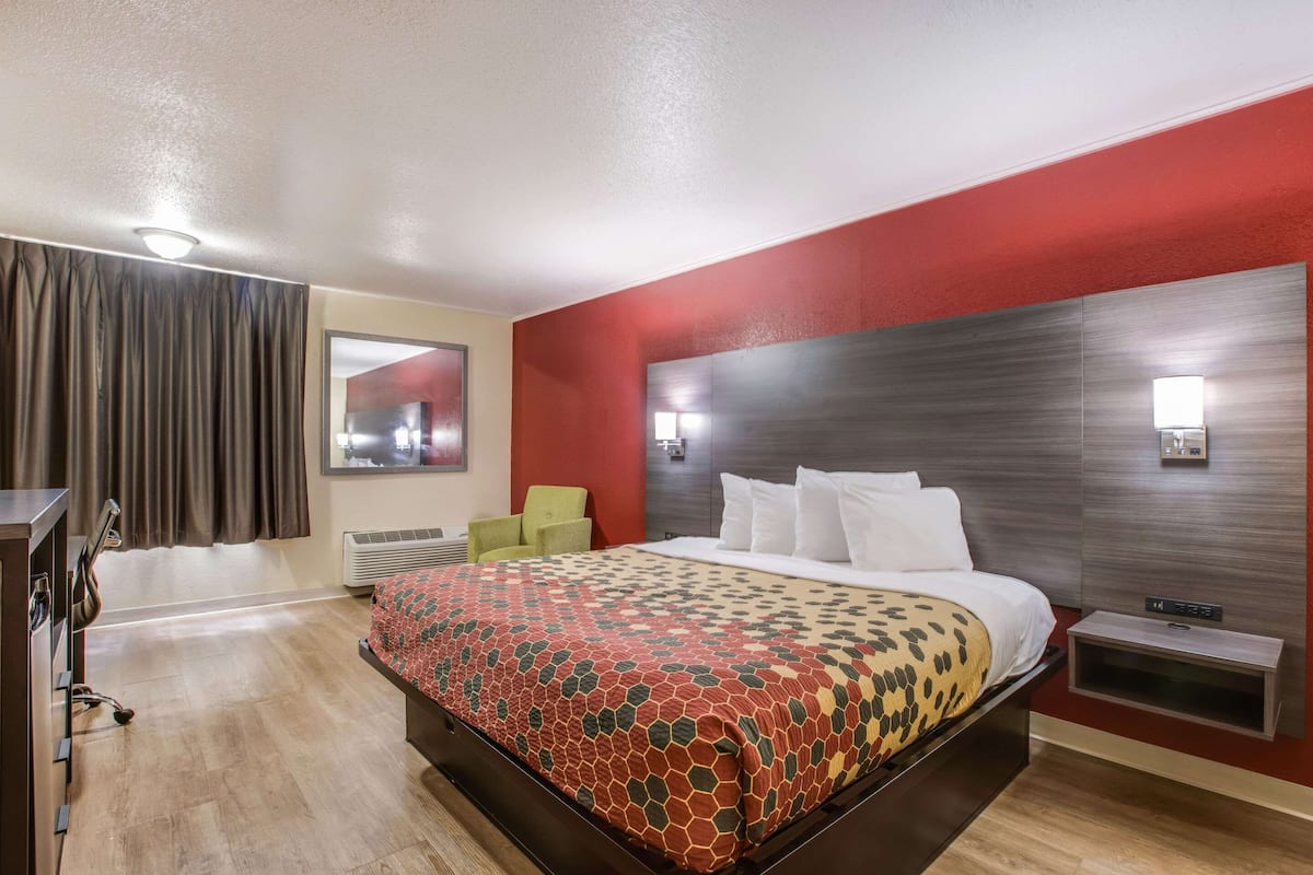Une chambre d’hôtel avec un grand lit, un bureau avec une chaise, une télévision et un mur d’accent de couleur rouge.