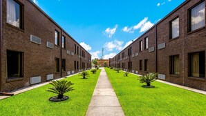 Um caminho ladeado por edifícios de tijolo, com pequenas árvores e céu claro.