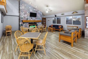 Un área de comedor con sillas y mesas de madera, una pared de piedra, una chimenea y un televisor montado en la pared.